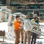 Stage crew carrying truss during outdoor LED stage load-in with road cases