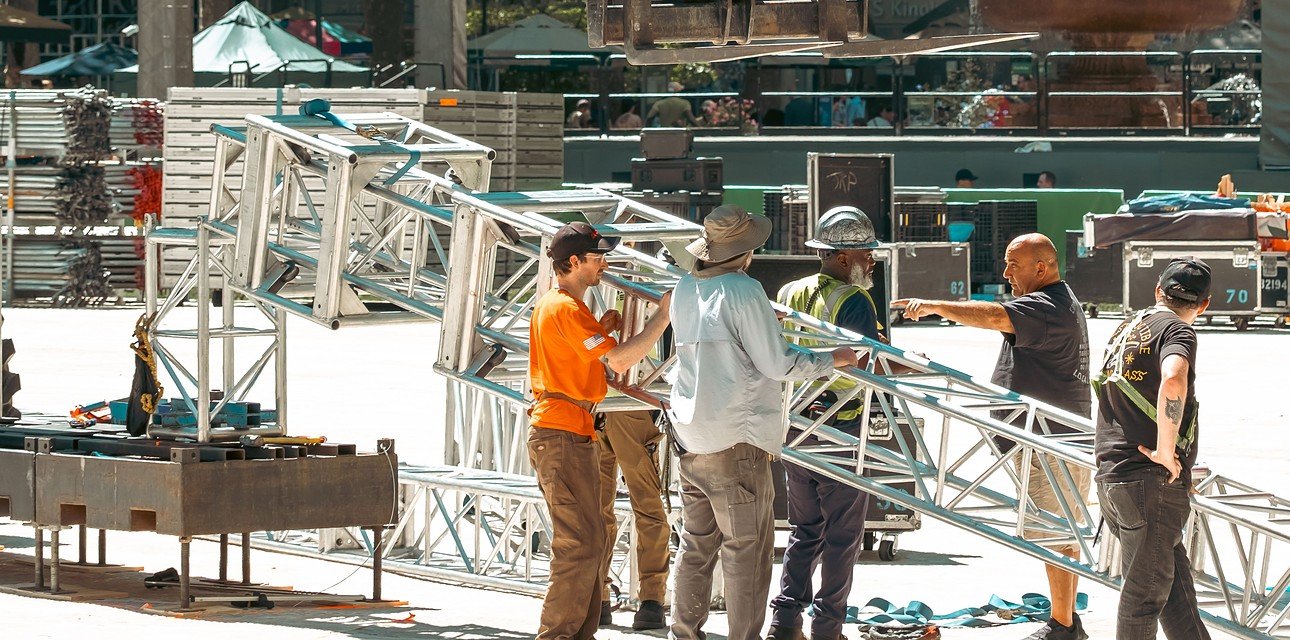 Stage crew carrying truss during outdoor LED stage load-in with road cases